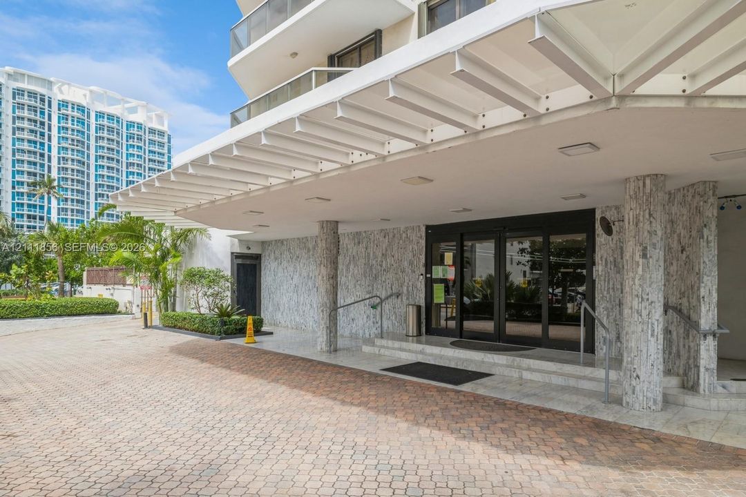 Covered entrance featuring a stone-clad facade, paver driveway, recessed lighting, and metal handrails