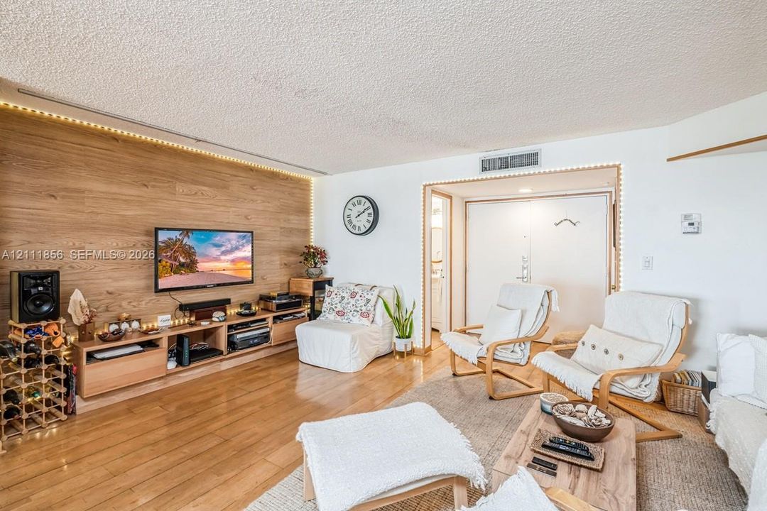 Living area featuring wood-finish flooring, a wood-paneled accent wall with integrated ambient lighting, and a built-in media console