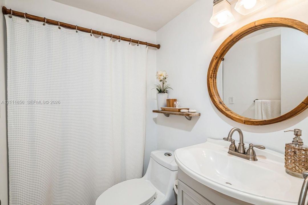 Bathroom vanity with a white basin and metallic faucet, circular wood-framed mirror, dual-bulb wall-mounted light fixture, and wooden wall-mounted shelving