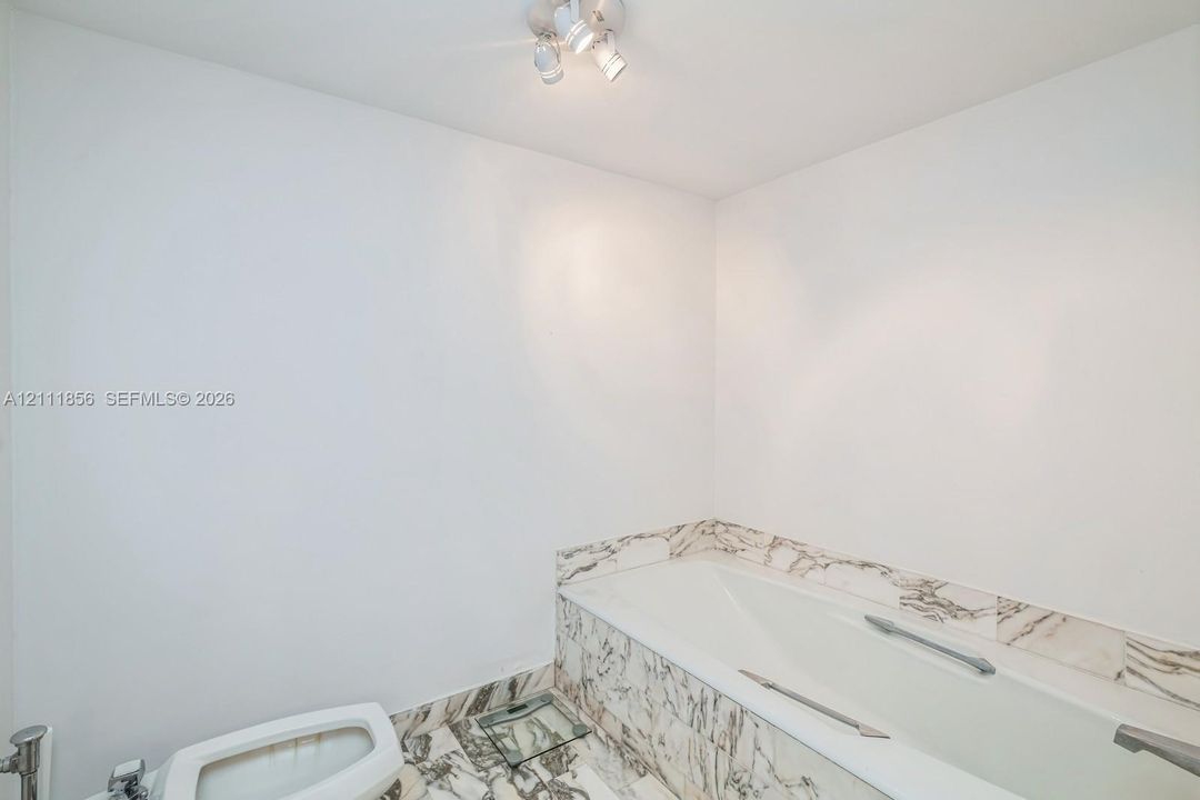 Bathtub featuring stone-patterned tile surround and flooring, accompanied by polished chrome hardware and a ceiling-mounted spotlight fixture