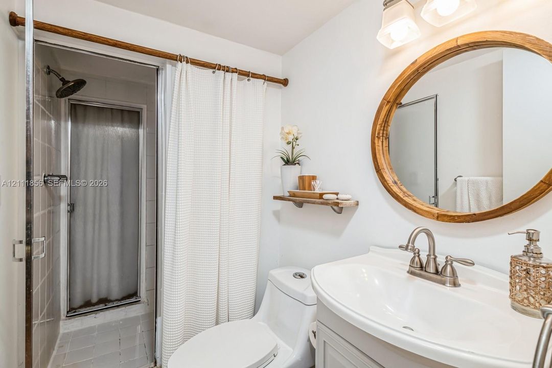 Bathroom featuring a vanity with an integrated basin, oval wood-frame mirror, wall-mounted floating shelf, and a shower enclosure with tile surround and fixed shower head