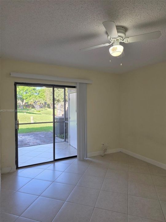 Interior space featuring diagonal ceramic tile flooring, a white ceiling fan with integrated lighting, and a sliding glass door opening to a paved, screened-in patio