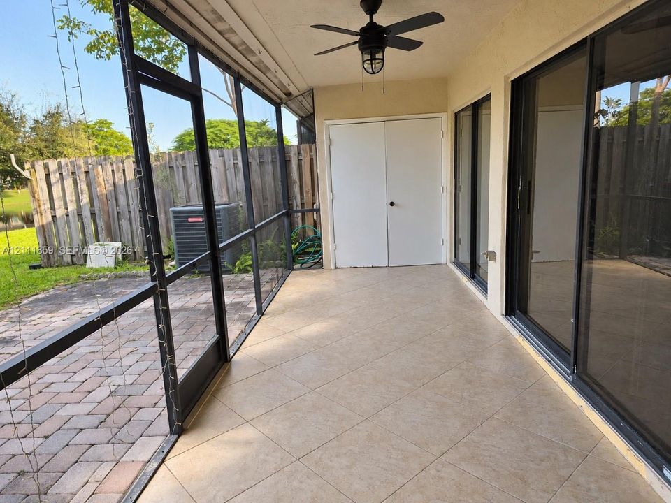 Screened-in patio featuring tile flooring, dual glass sliding doors, a ceiling fan, and double-door storage