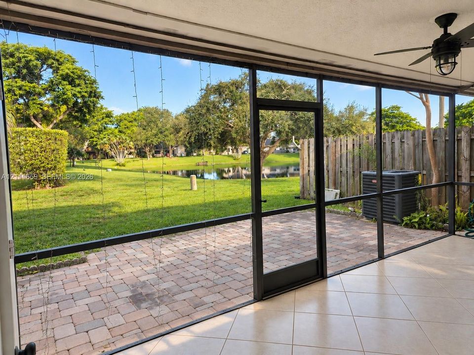 Screened-in patio with tiled flooring and ceiling-mounted fan, featuring brick-paver hardscaping, mature landscaping, and waterfront scenery