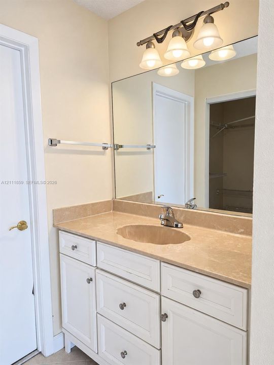 White cabinetry vanity with stone-style countertop and integrated sink, full-width mirror, and four-light fixture