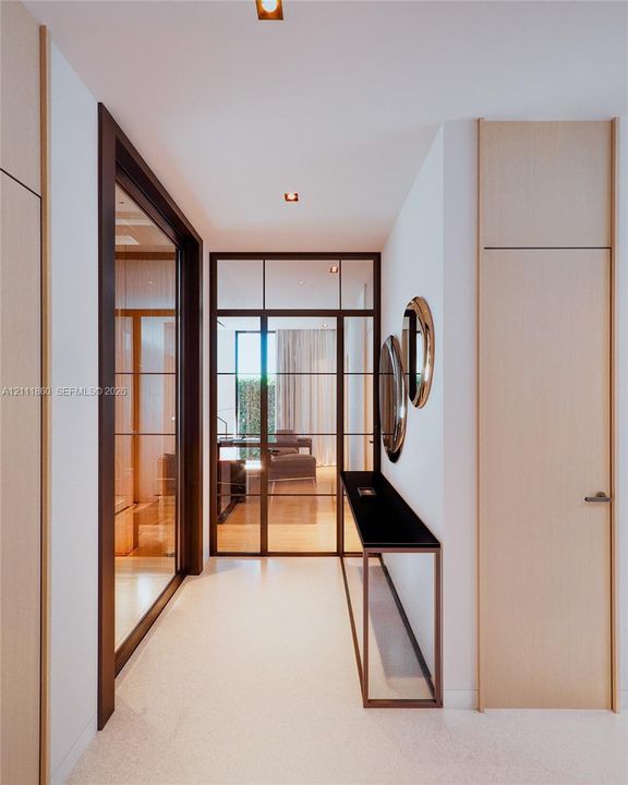 Hallway featuring full-height light wood doors, a metal-framed glass partition with a paneled door, flush-mount ceiling lighting, and a built-in wall-mounted console with a dark stone surface
