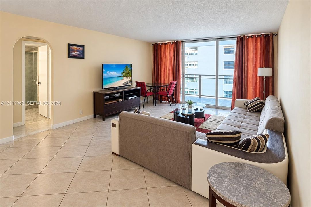 Open-concept living area featuring light-toned tile flooring, an arched entryway, and large sliding glass doors providing access to a private balcony