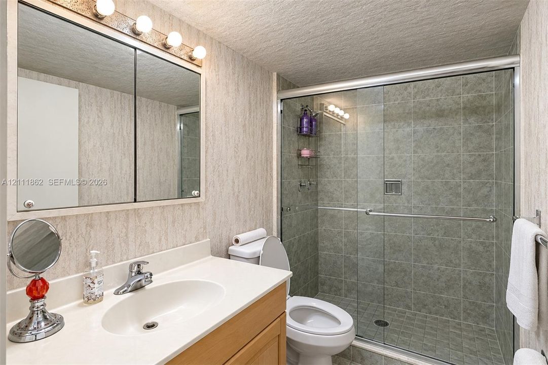 Bathroom featuring a wood-finish vanity with a solid-surface countertop, an integrated sink, a mirrored medicine cabinet with integrated lighting, and a walk-in shower with a glass sliding door and tiled surround