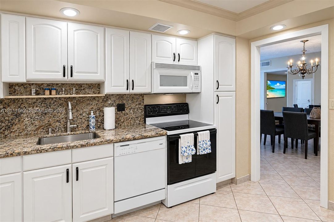 Kitchen featuring white shaker-style cabinetry, stone-finish countertops, stainless steel undermount sink, built-in microwave, and recessed lighting