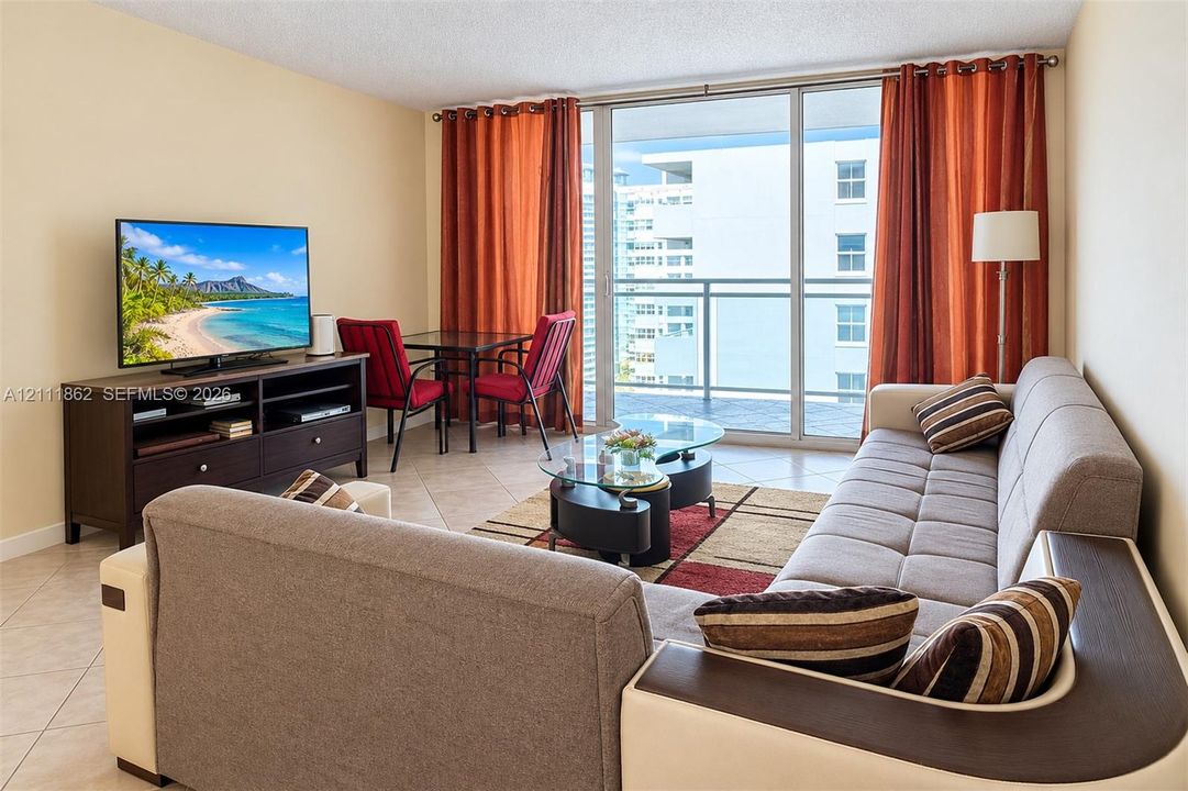 Living space featuring large-format ceramic tile flooring, floor-to-ceiling glass sliding doors, and a private balcony with metal railing