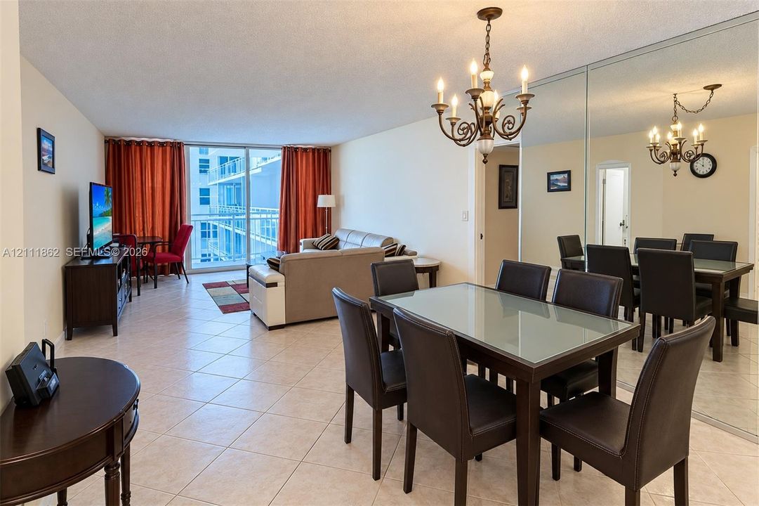 Open-concept floor plan featuring tile flooring, a floor-to-ceiling mirrored wall, iron-style chandelier, and glass balcony door