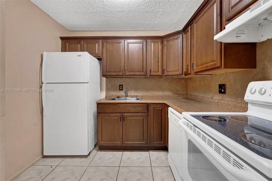 Kitchen featuring wood cabinetry, stone-texture tile backsplash, laminate countertops, and tile flooring