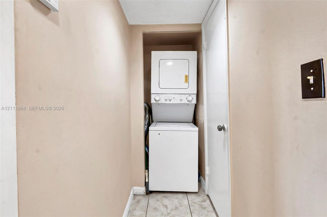 Utility closet featuring a stacked washer and dryer unit and tile flooring