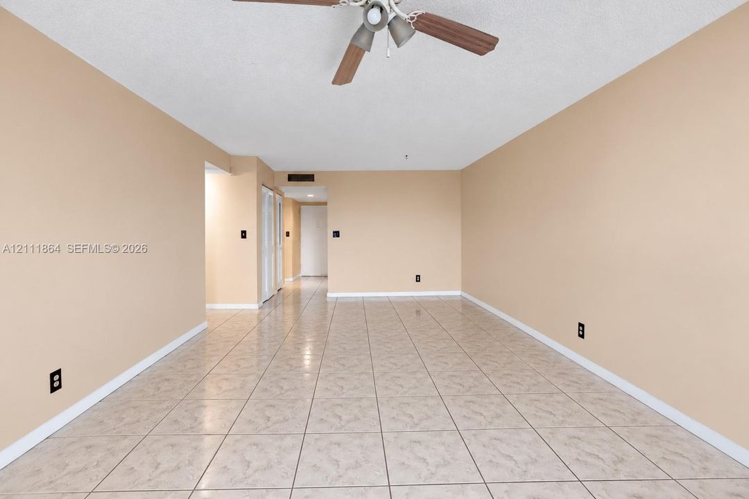 Spacious room featuring neutral wall paint, tiled flooring, and a ceiling-mounted light fixture with a fan