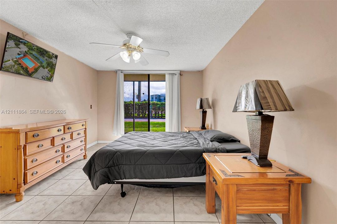 Bedroom featuring large-format tile flooring, a ceiling fan with integrated lighting, and a sliding glass door providing exterior access