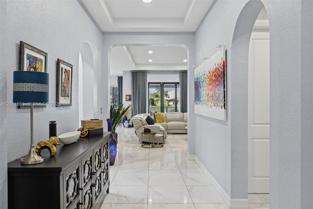 Entryway featuring large-format tile flooring, recessed tray ceiling, and prominent arched architectural openings