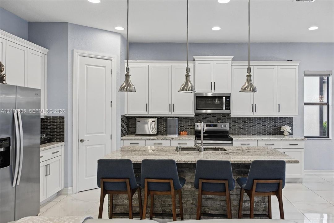 Beautiful kitchen featuring white shaker-style cabinetry, & stone-surface center island & stylish over counter pendant lighting.