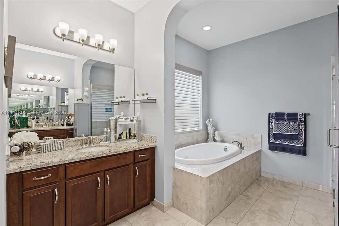 Master Bathroom featuring rich wood cabinetry and stone countertop + soaking tub.