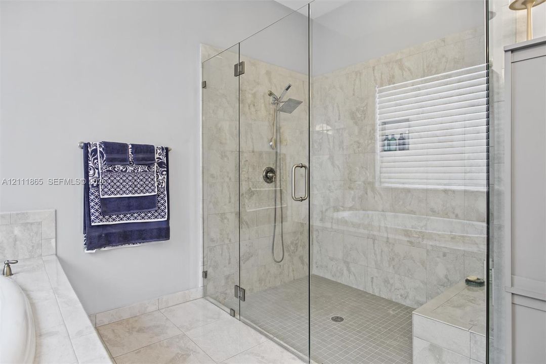 Large master walk-in shower with frameless glass enclosure, natural stone wall tile and integrated bench.