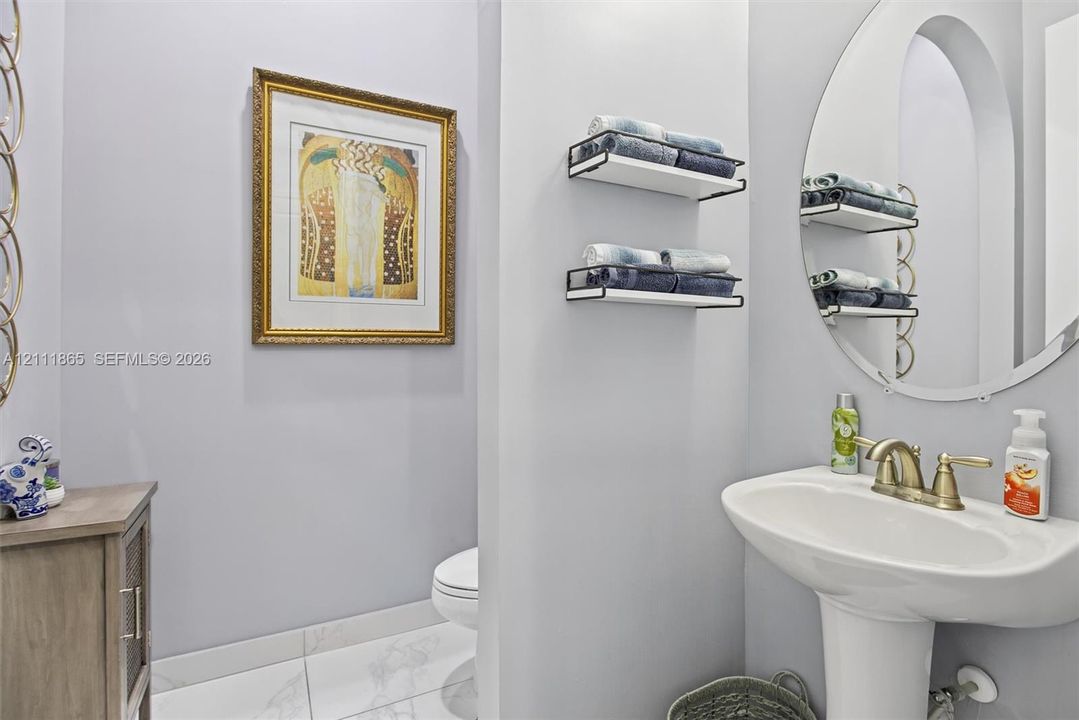 Chique powder room featuring white pedestal sink, metallic finish faucet, oval mirror & wall-mounted shelving.