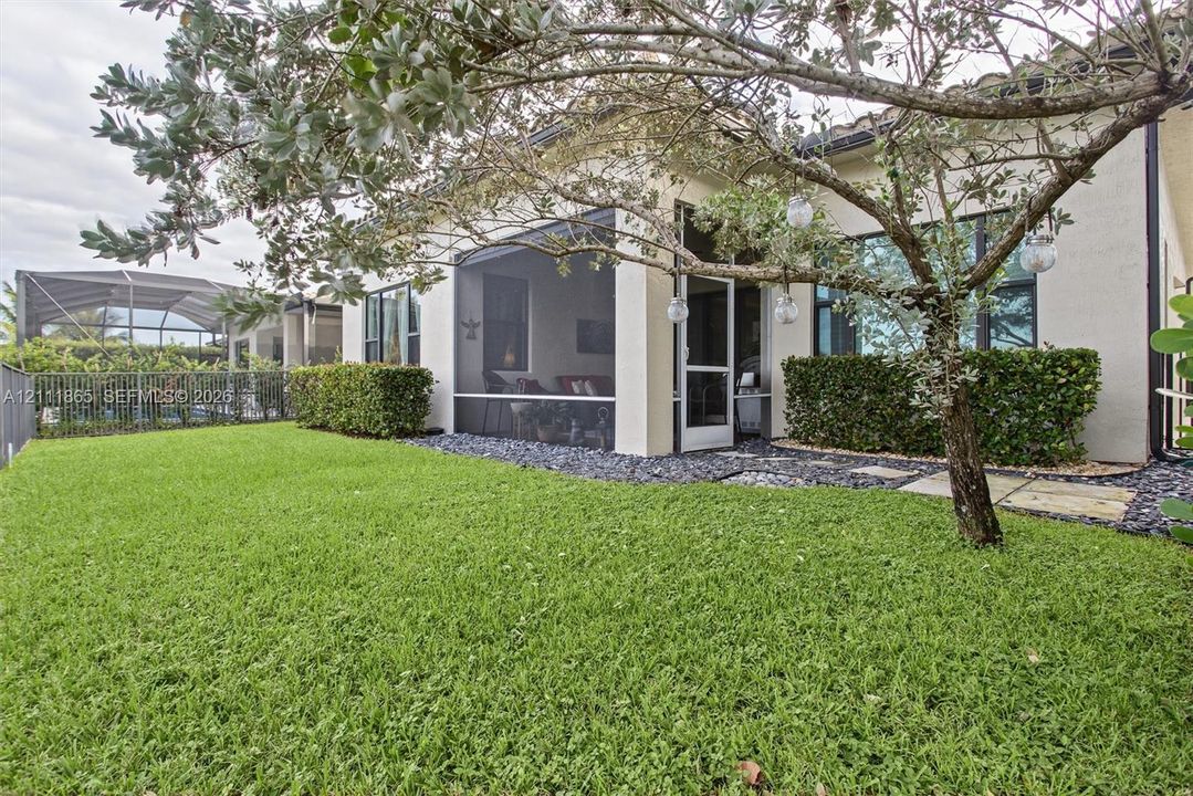 Back yard perspective. Notice lawn, dark stone landscape border, and shade tree