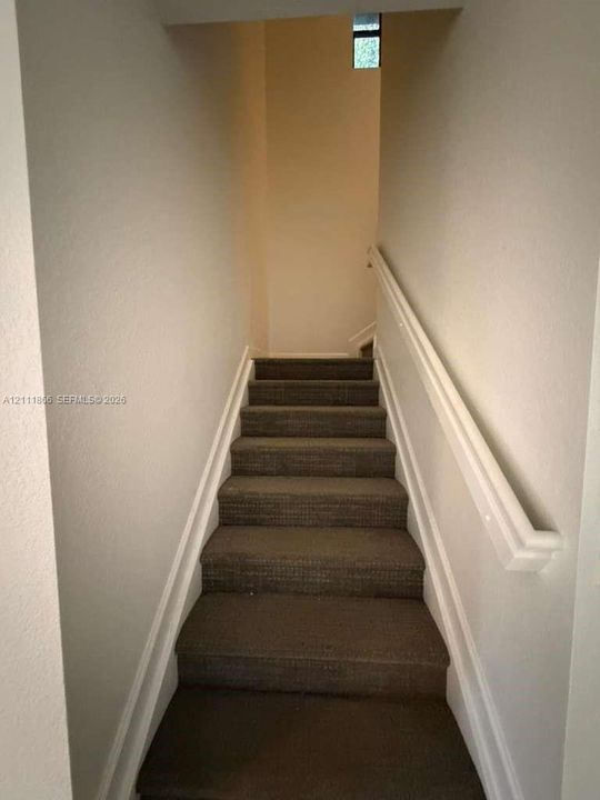 Staircase featuring textured carpeted treads and a mounted white handrail