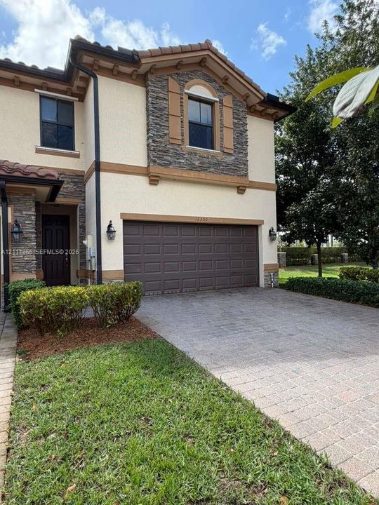 Two-story exterior featuring a stone facade, stucco siding, a tiled roof, a paved driveway, and wall-mounted exterior lighting