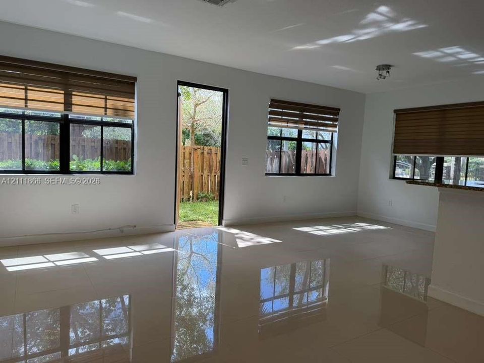 Interior space featuring large-format tile flooring, multiple windows with integrated blinds, and an exterior door providing access to a fenced yard