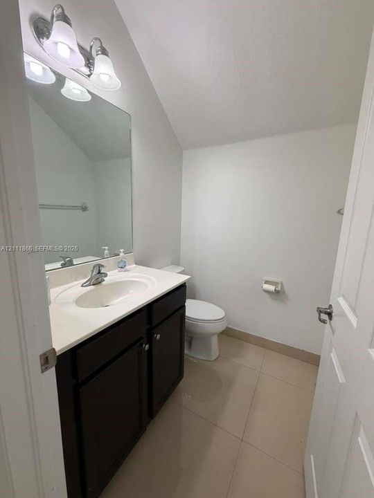 Bathroom featuring a vanity with dark cabinetry, solid-surface countertop, integrated oval sink, full-width wall mirror, and dual-bulb vanity light