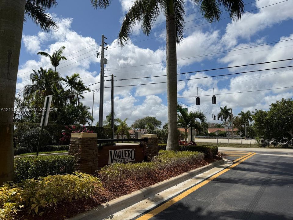 Community entrance monument featuring stacked stone pillars, integrated wood-finish signage, and manicured tropical landscaping with mature palm trees