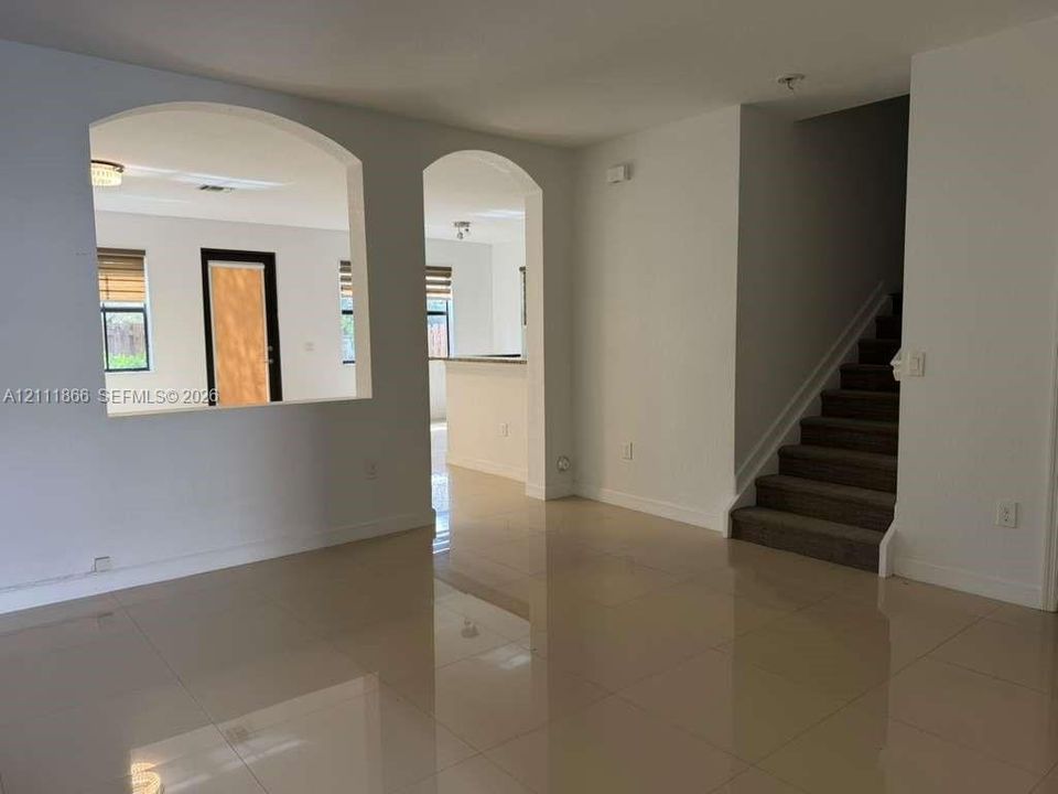 Interior featuring arched architectural pass-throughs, large-format tile flooring, and carpeted staircase