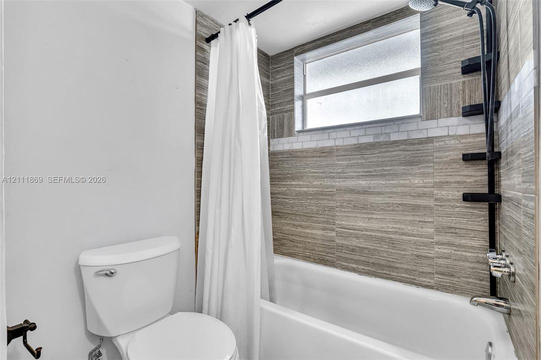 Full bathroom featuring a tub-shower combination with horizontal wood-finish tile surround, a decorative mosaic accent border, a black matte hardware rainfall shower head, and an obscure glass window
