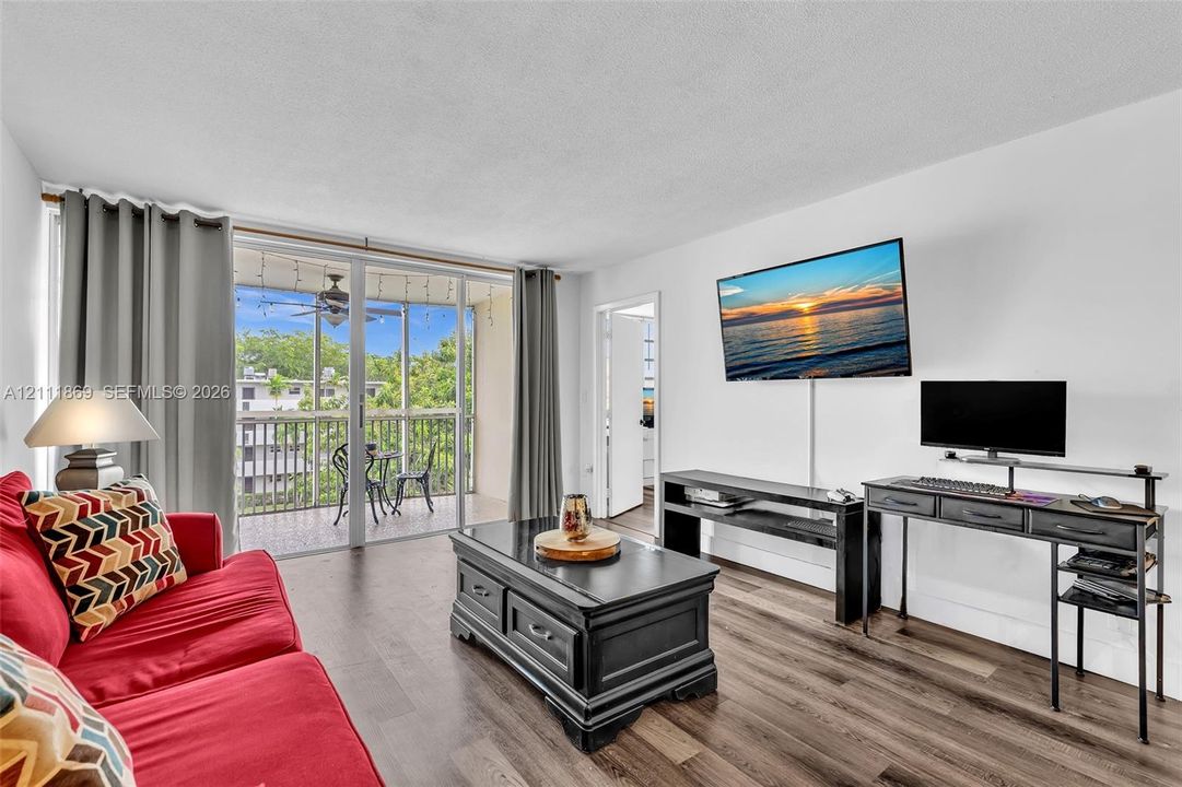 Living area featuring wood-finish flooring, floor-to-ceiling glass sliding doors, and a screened-in balcony