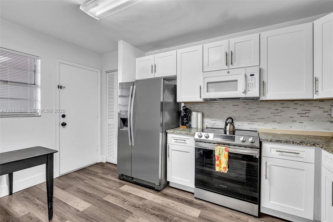 Kitchen featuring white shaker-style cabinetry, stainless steel appliances, speckled stone-finish countertops, linear tile backsplash, and wood-finish flooring