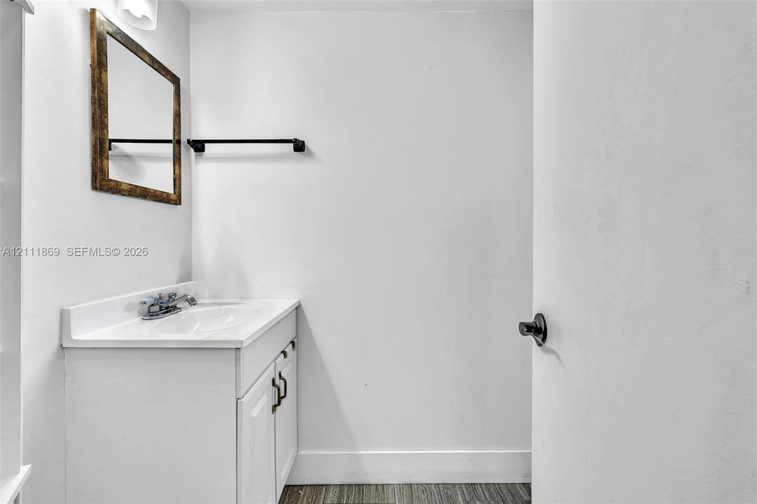White vanity cabinet with an integrated sink and countertop, framed rectangular wall mirror, matte black towel bar, and wood-finish flooring