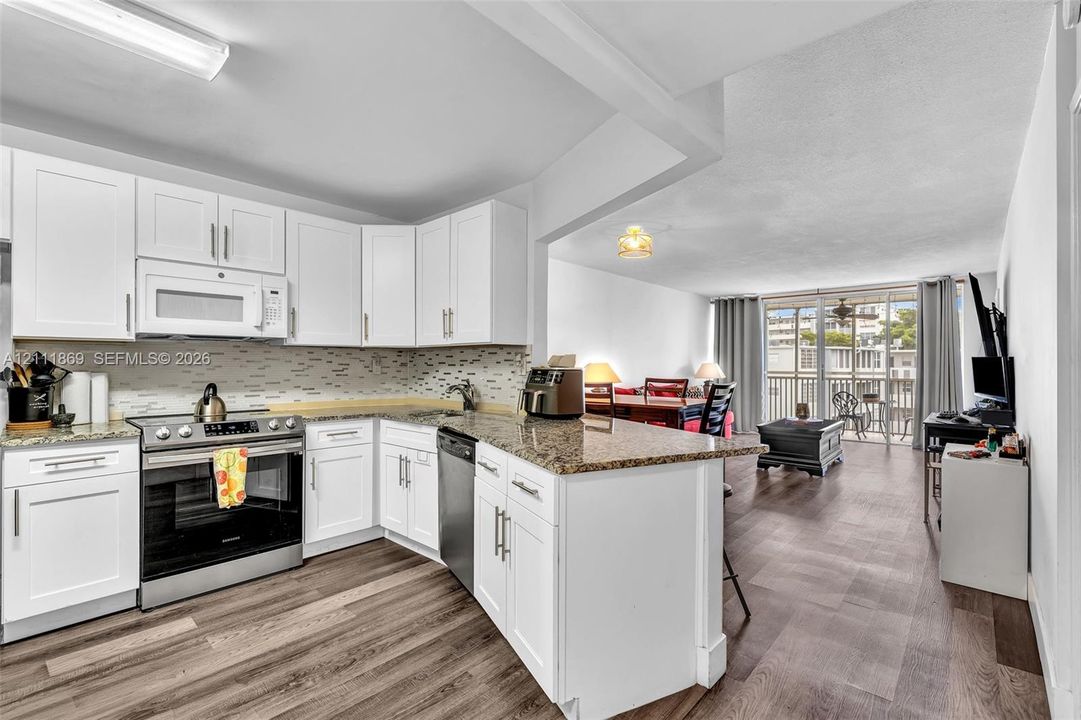 Kitchen featuring white shaker-style cabinetry, stone countertops, stainless steel appliances, a tile backsplash, and wood-finish flooring