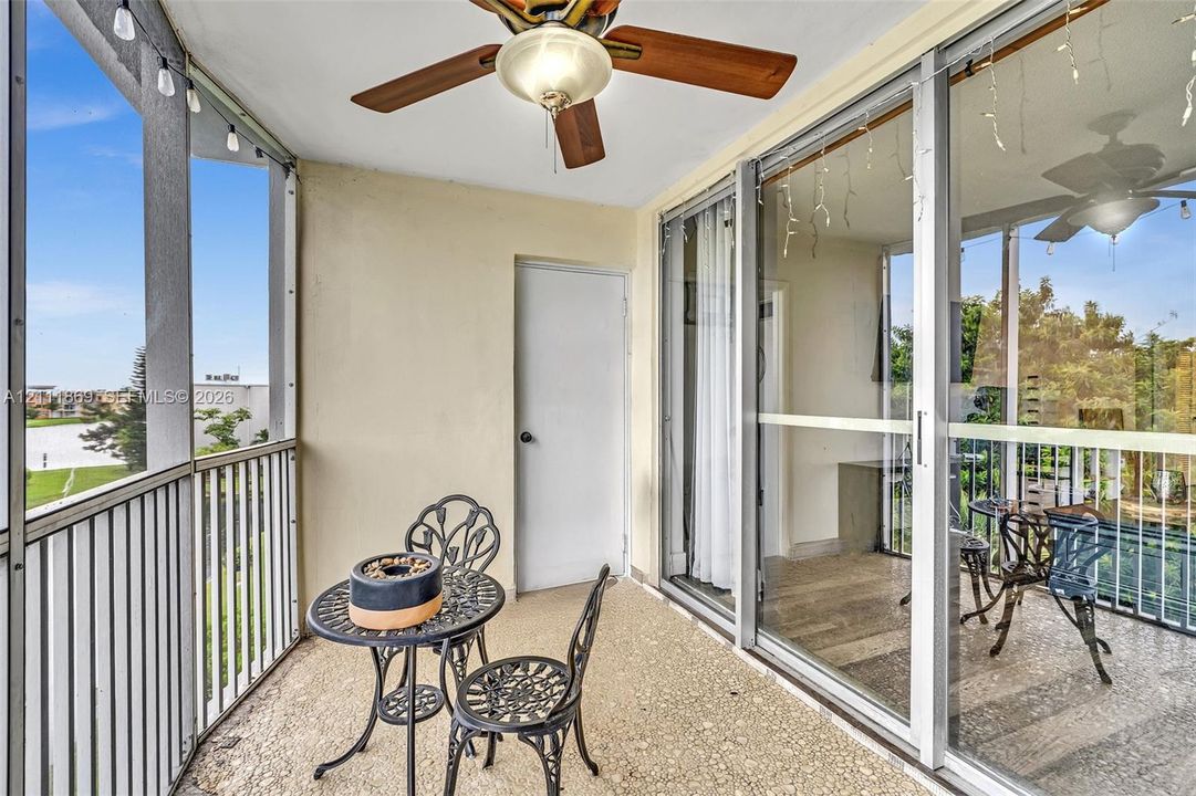 Screened-in balcony featuring a textured concrete floor, ceiling fan with light fixture, metal railings, and floor-to-ceiling sliding glass doors