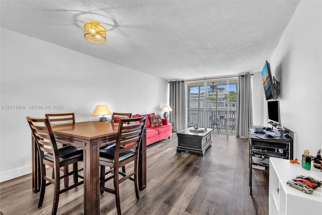 Wood-finish flooring, textured ceiling, flush-mount circular lighting fixture, and floor-to-ceiling glass sliding doors opening to a private balcony