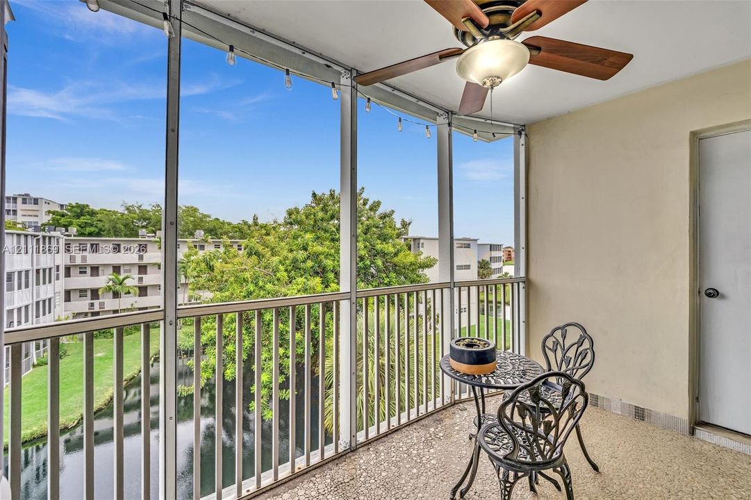 Screened balcony featuring a white metal frame, terrazzo flooring, built-in ceiling fan with light fixture, and string lighting