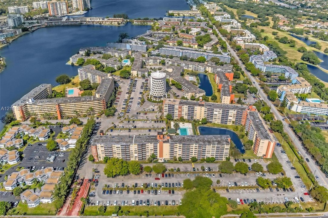 Aerial perspective of a multi-building residential complex featuring on-site swimming pools, waterfront positioning, expansive parking areas, and landscaped grounds