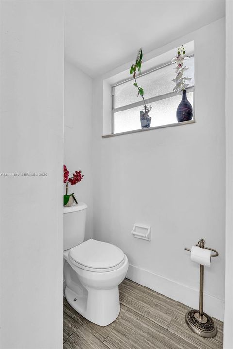 Restroom featuring a dual-pane privacy glass window, porcelain toilet, and wood-finish flooring