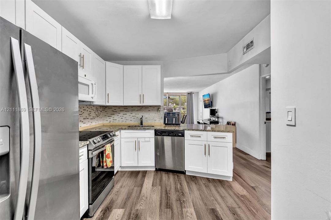 Kitchen featuring white shaker-style cabinetry, stone-surface countertops, stainless steel appliances, a multi-tonal mosaic tile backsplash, and wood-finish flooring