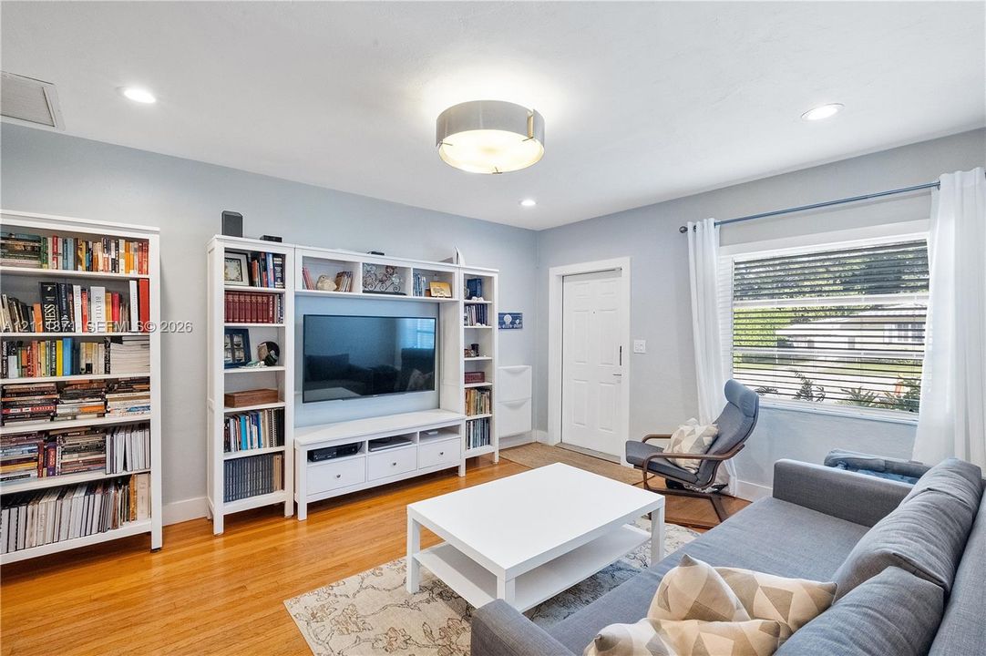 Living area featuring hardwood flooring, built-in white cabinetry, recessed lighting, and a multi-tiered ceiling fixture