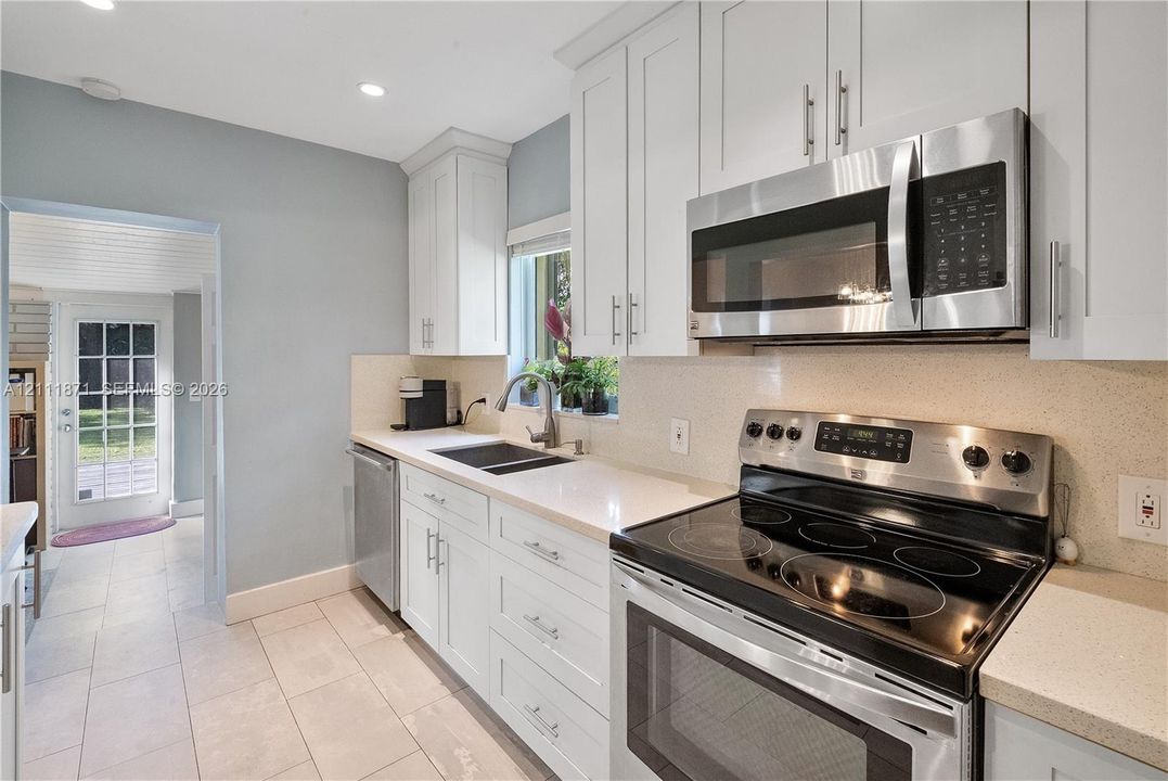 Kitchen featuring white shaker-style cabinetry, light-toned stone countertops, stainless steel appliances, a deep undermount sink, and tiled flooring