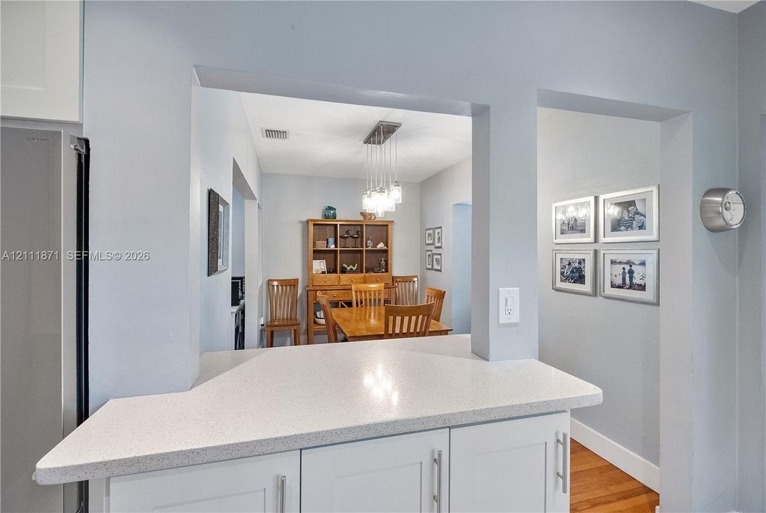 White cabinetry with shaker-style doors, quartz countertop, and multi-light linear pendant fixture