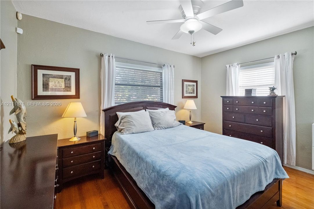 Room featuring wood-finish flooring, two windows with horizontal blinds, and a white ceiling fan with integrated lighting