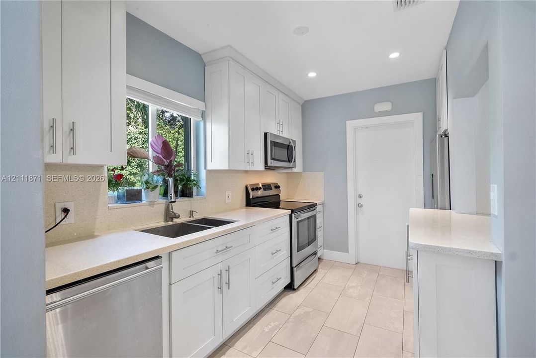 Kitchen featuring white shaker-style cabinetry, stainless steel appliances, neutral stone-finish countertops, tile flooring, and a dual-basin sink with a pull-down faucet