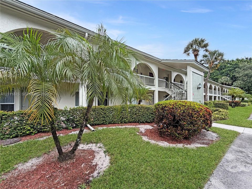 Stucco exterior featuring arched architectural detailing, covered balconies, and landscaped grounds with mature palm trees