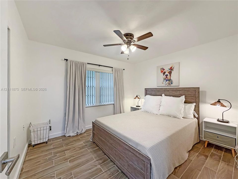 Neutral-toned room featuring wood-finish tile flooring, a multi-blade ceiling fan with integrated lighting, and a single window with vertical blinds