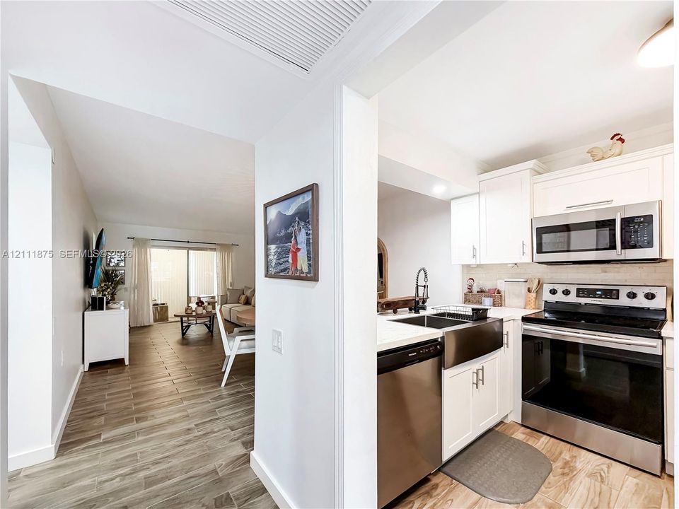 Kitchen featuring white cabinetry, stainless steel appliances, a farmhouse-style sink, and wood-finish flooring